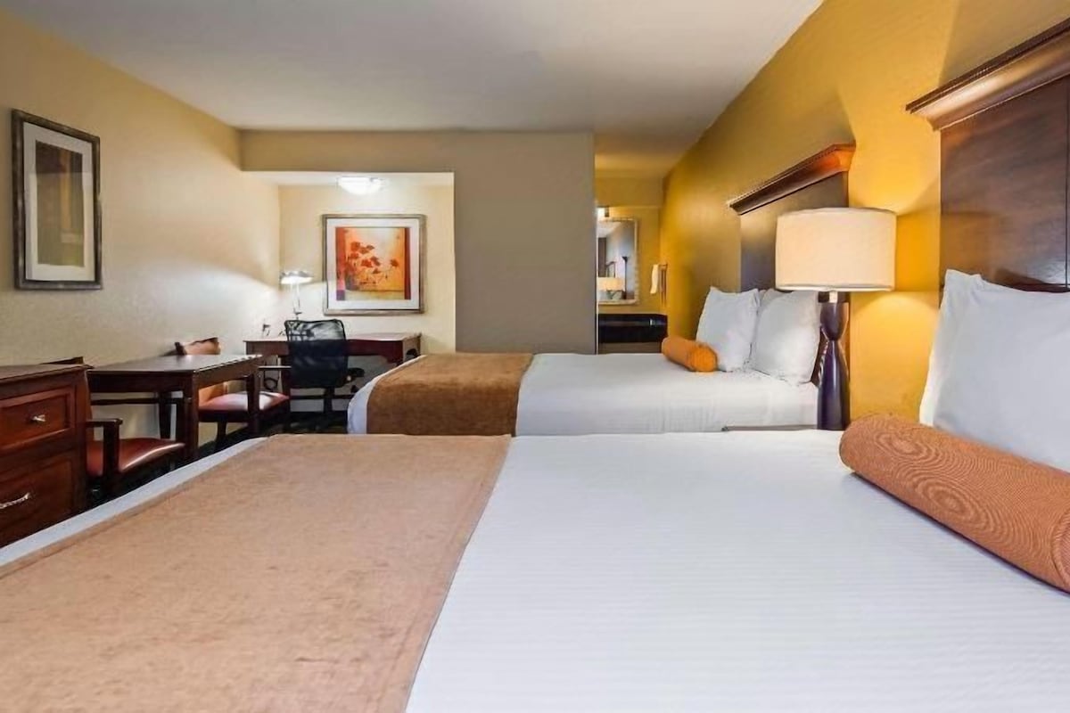 A hotel room with two beds, a desk, a chair, and a lamp.