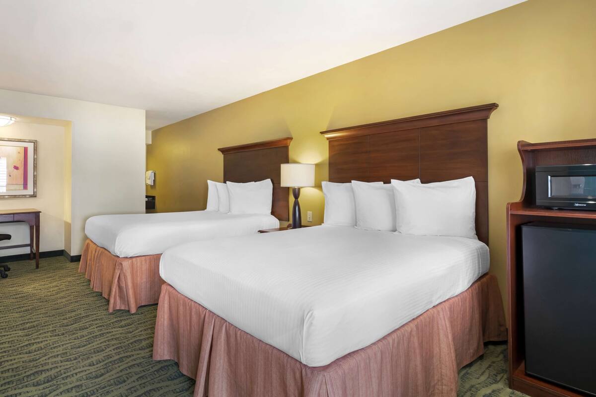 A hotel room with two beds, a desk, a lamp, and a television.