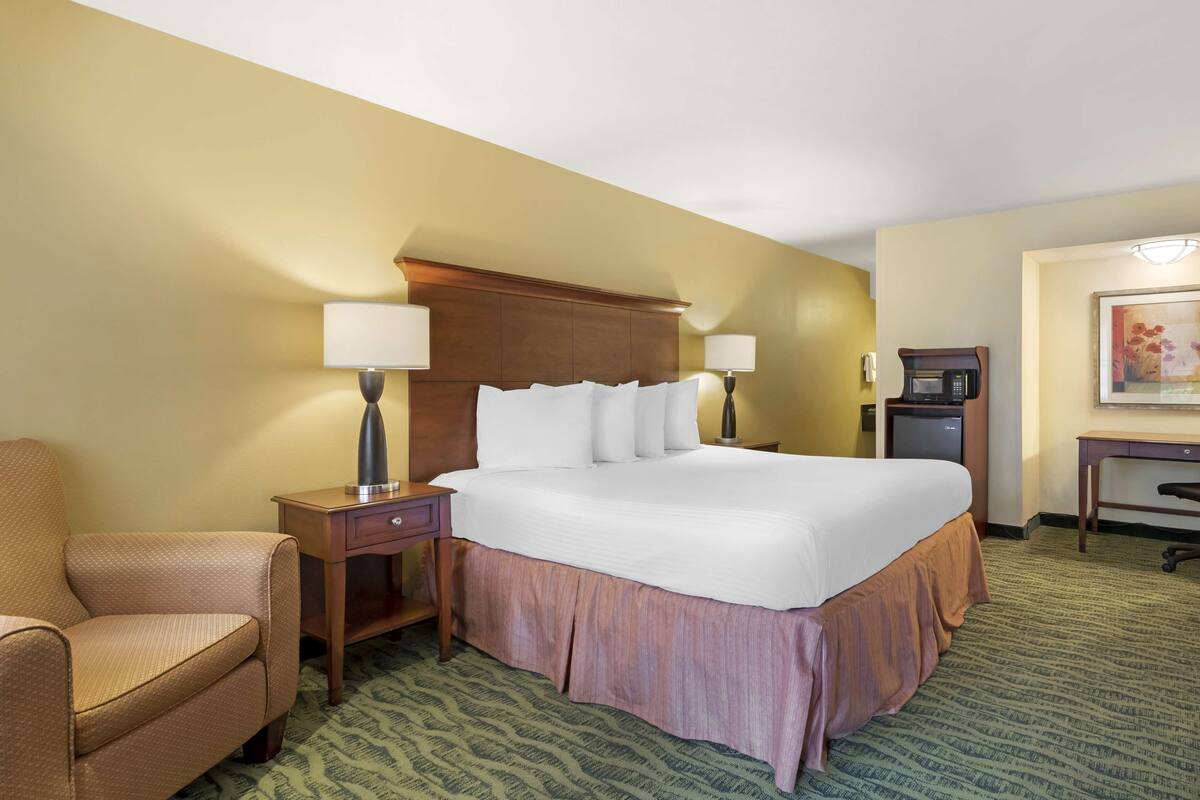 A hotel room with a large bed, two bedside tables with lamps, a desk, a chair, and a coffee machine.