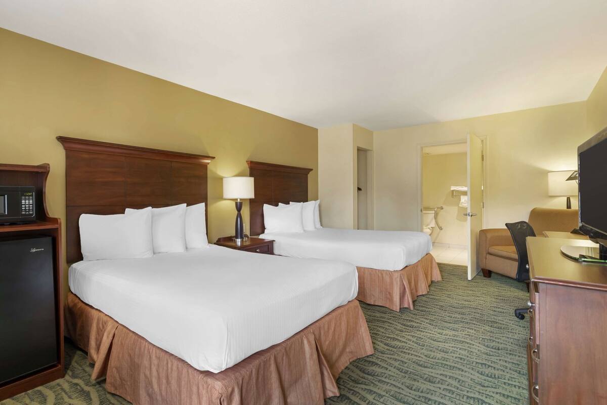 A hotel room with two beds, a desk, a television, and a microwave.