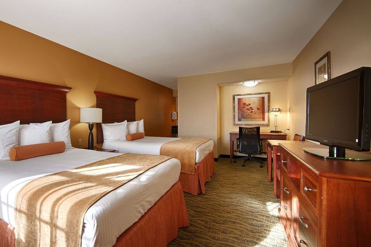 A hotel room with two beds, a desk, a television, and a chair.