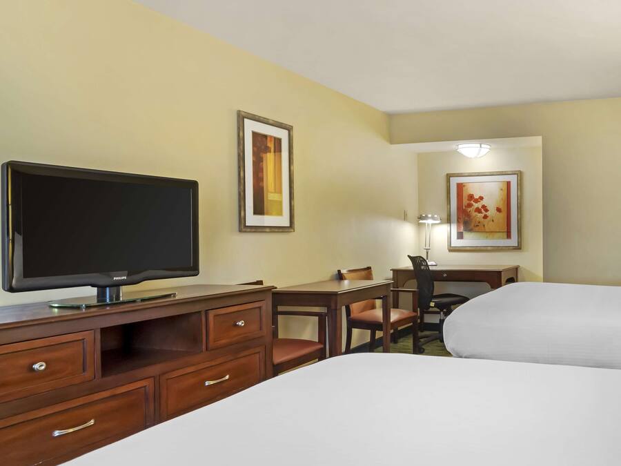 Een hotelkamer met een flatscreen televisie, een bureau met een stoel, een bed en twee ingelijste foto's aan de muur.