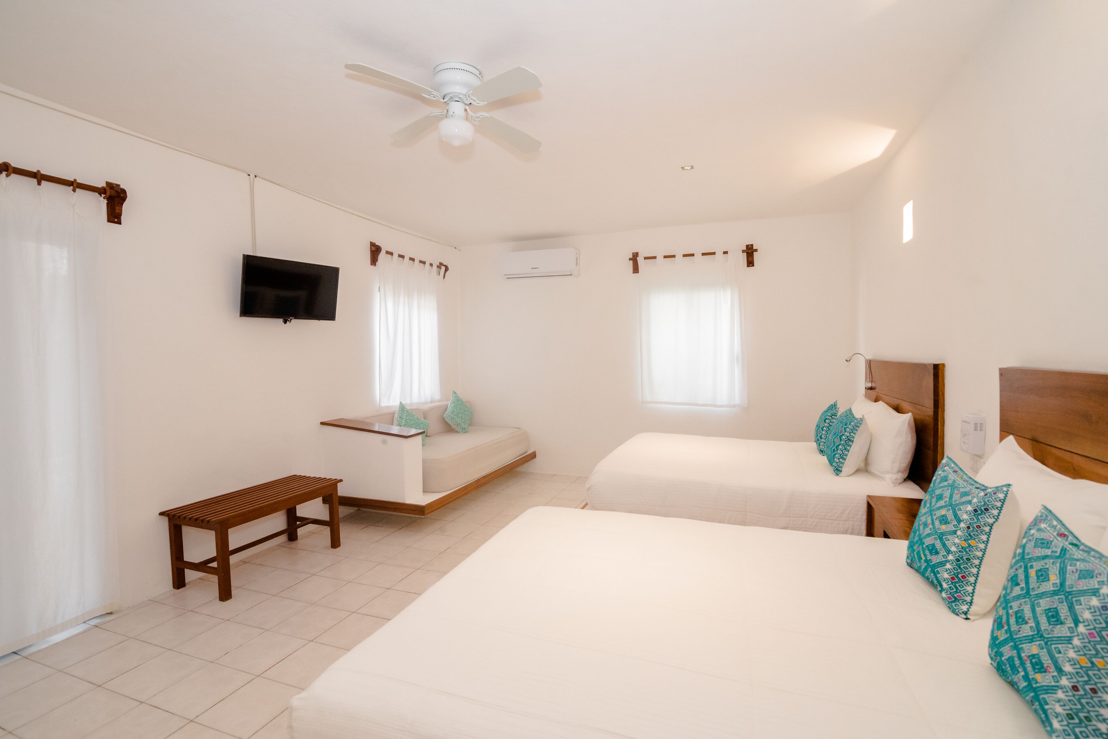 A bedroom with two beds, a TV, a ceiling fan, and a bench.