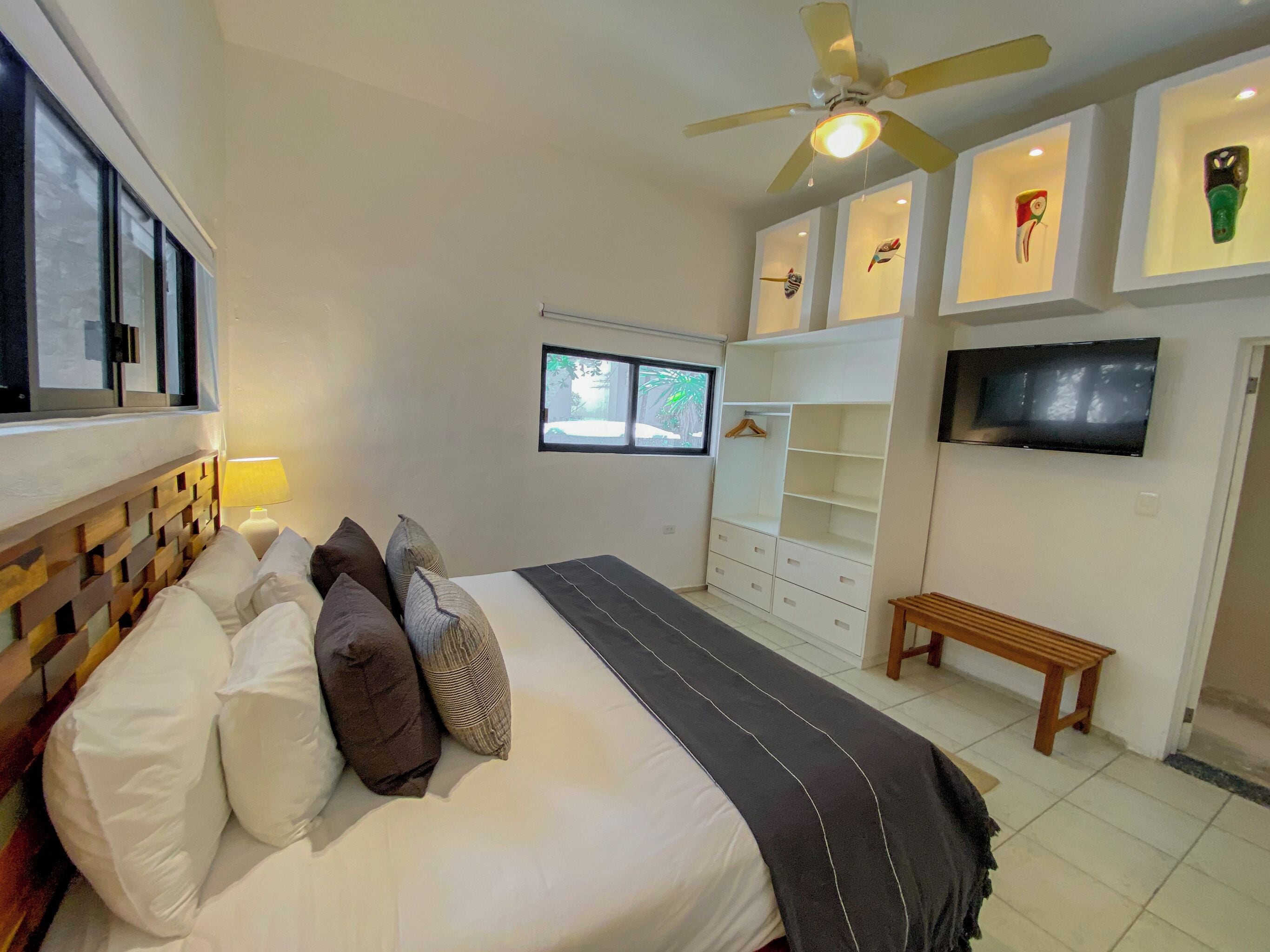 A bedroom with a bed, a ceiling fan, a TV, a wardrobe, and a window.
