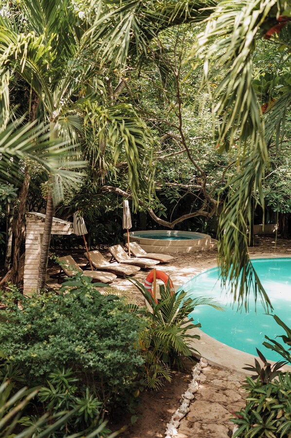 A pool area with lounge chairs and umbrellas, surrounded by lush greenery.