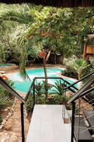 Uma área de piscina com escadaria dando acesso à piscina, cercada por plantas tropicais e uma estrutura de telhado de palha.