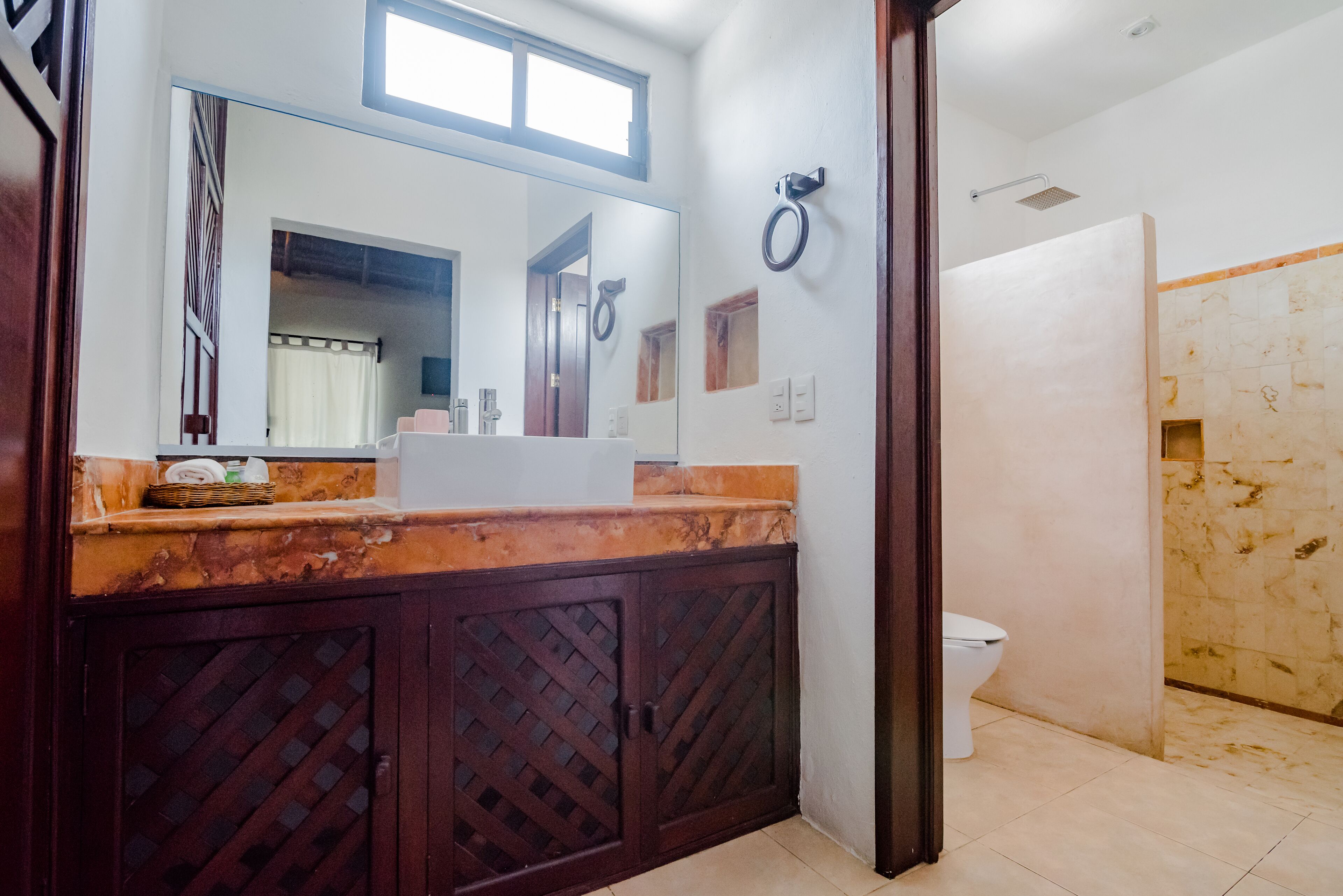 Un baño con tocador de madera, un espejo grande, ducha e inodoro.