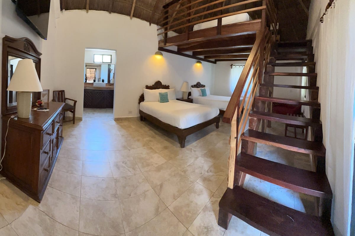 A spacious room with a wooden staircase, a bed, a desk, and a chair.