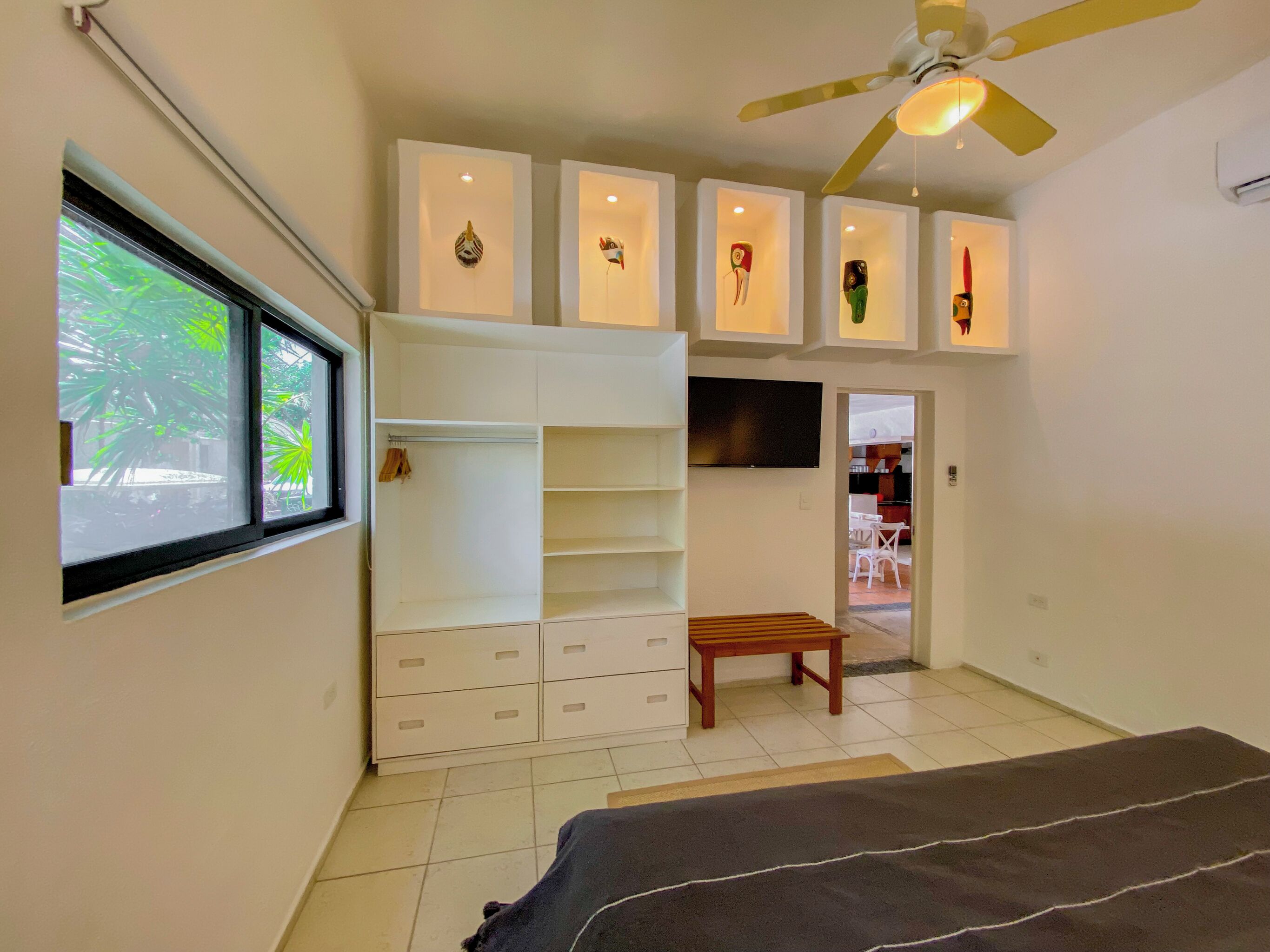 A bedroom with a bed, a wooden bench, a wardrobe, a TV, and a ceiling fan.
