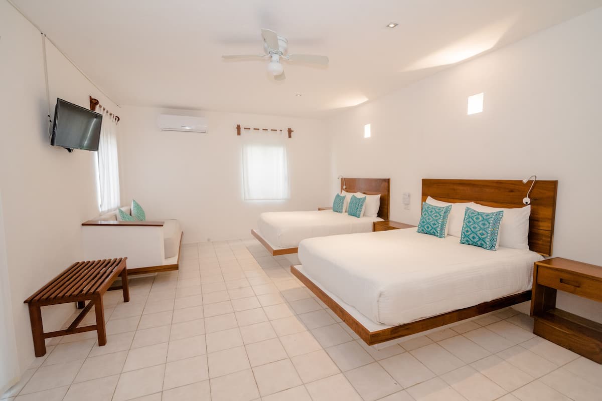 A hotel room with two beds, a TV, a ceiling fan, and a small wooden bench.