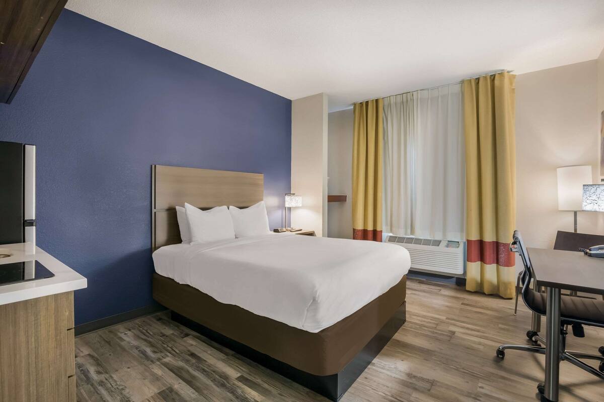 Una camera d'albergo con un letto, un comodino, una lampada e una scrivania con una sedia.
