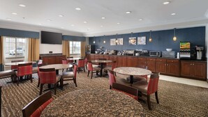 A hotel lobby with a seating area, a kitchen, and a large TV screen.