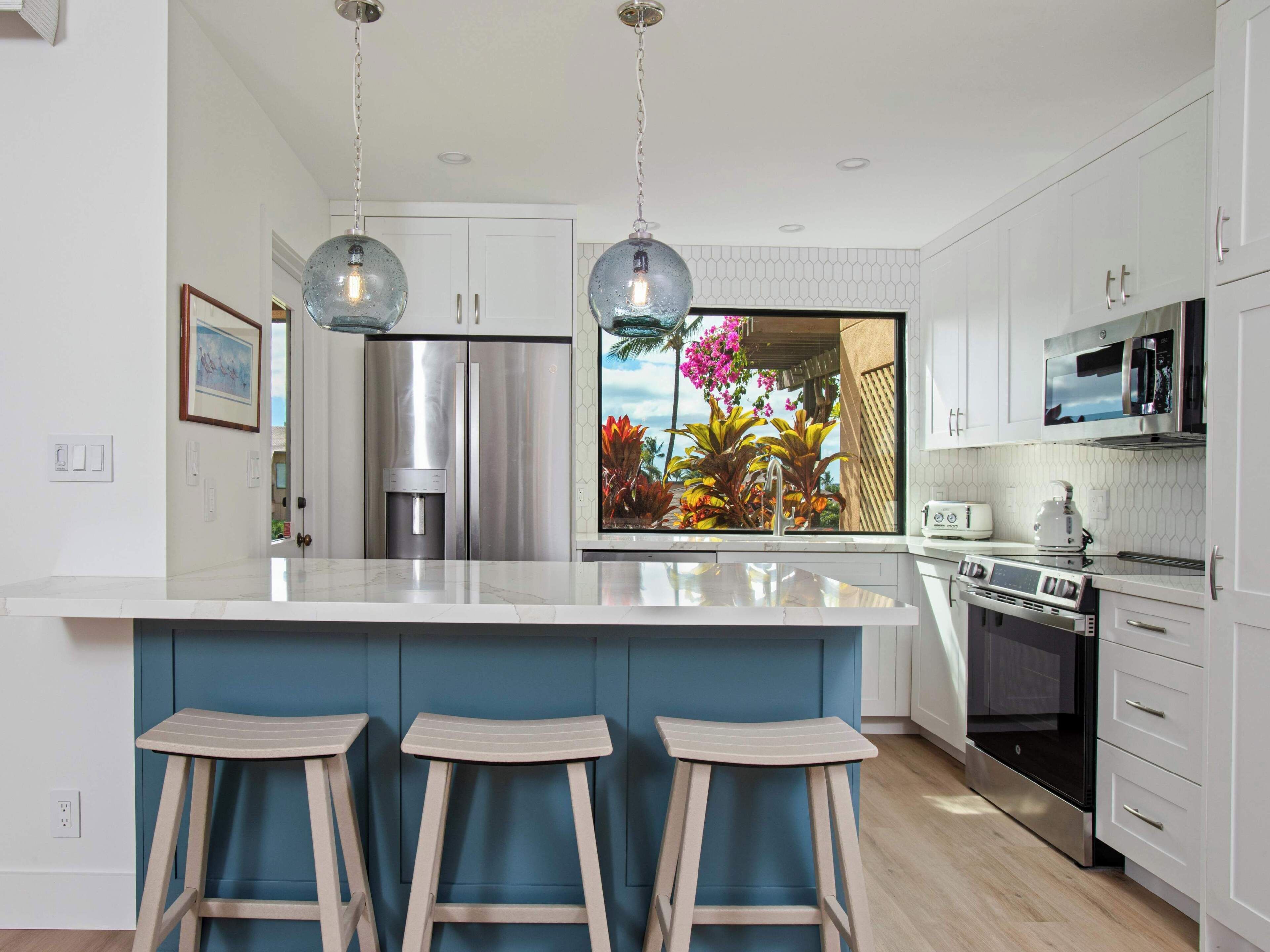 Una cocina moderna con una isla grande, electrodomésticos de acero inoxidable y vistas a plantas tropicales.