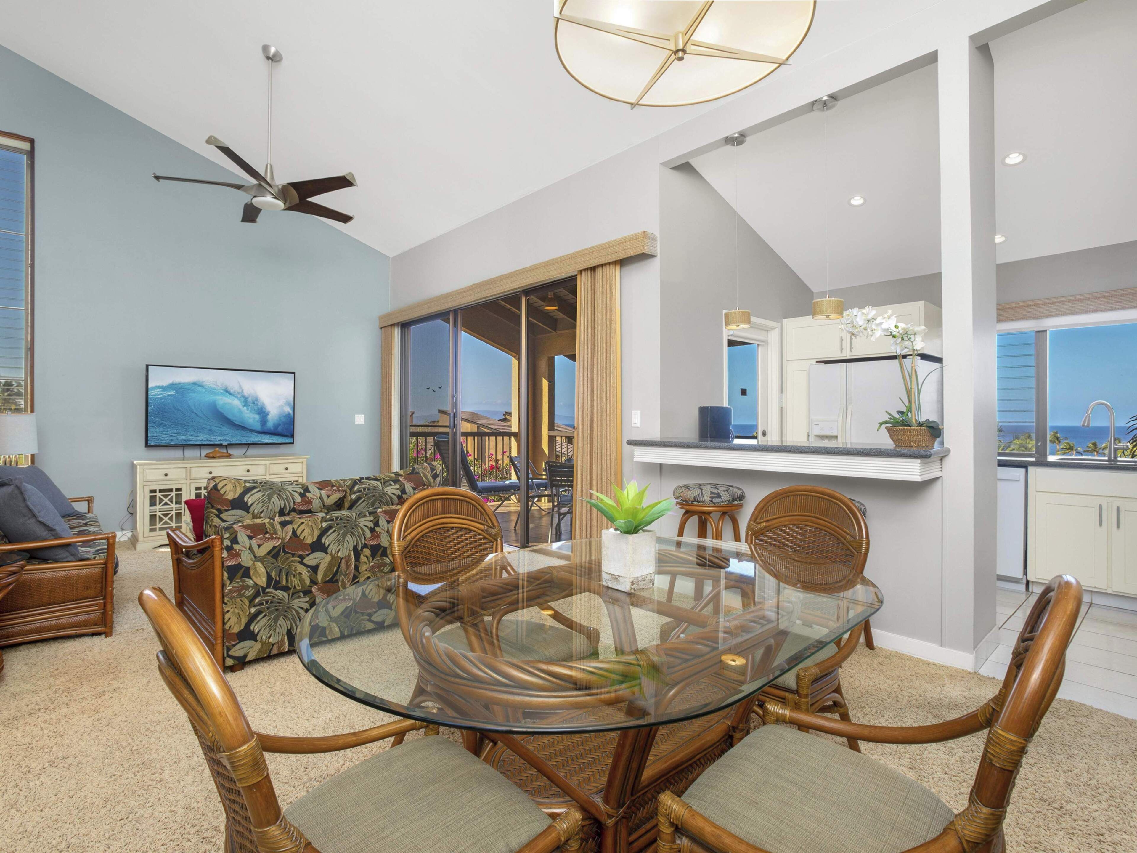A modern living room with a glass-top dining table surrounded by wicker chairs, a flat-screen TV, and a ceiling fan.