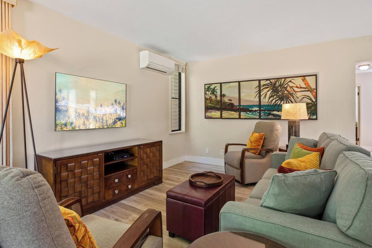 Una sala de estar con una televisión de pantalla plana, un mueble bajo de madera, un sofá, una silla y una lámpara de pie.