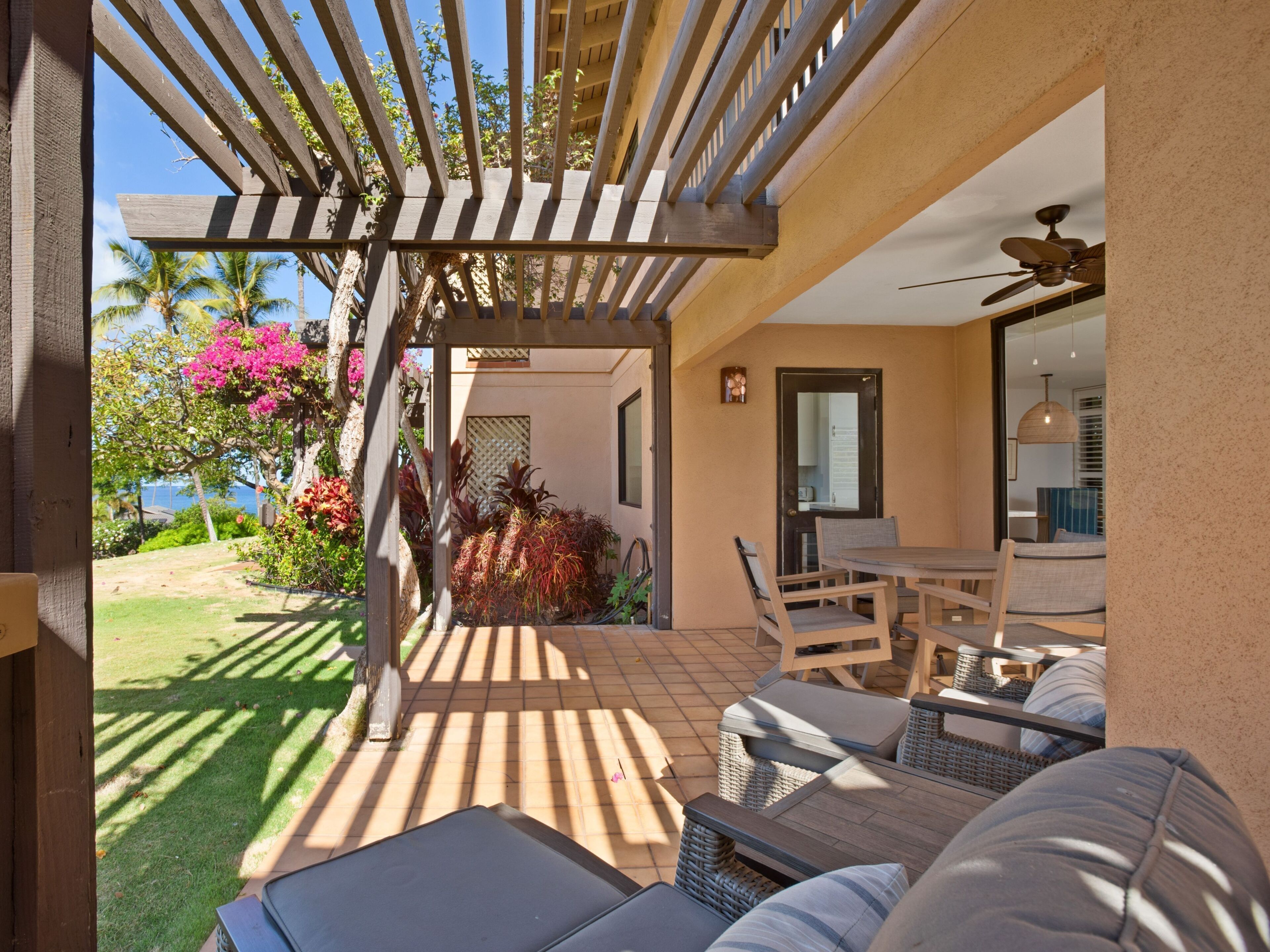 A patio with outdoor furniture, a pergola, and a view of the garden and sea.