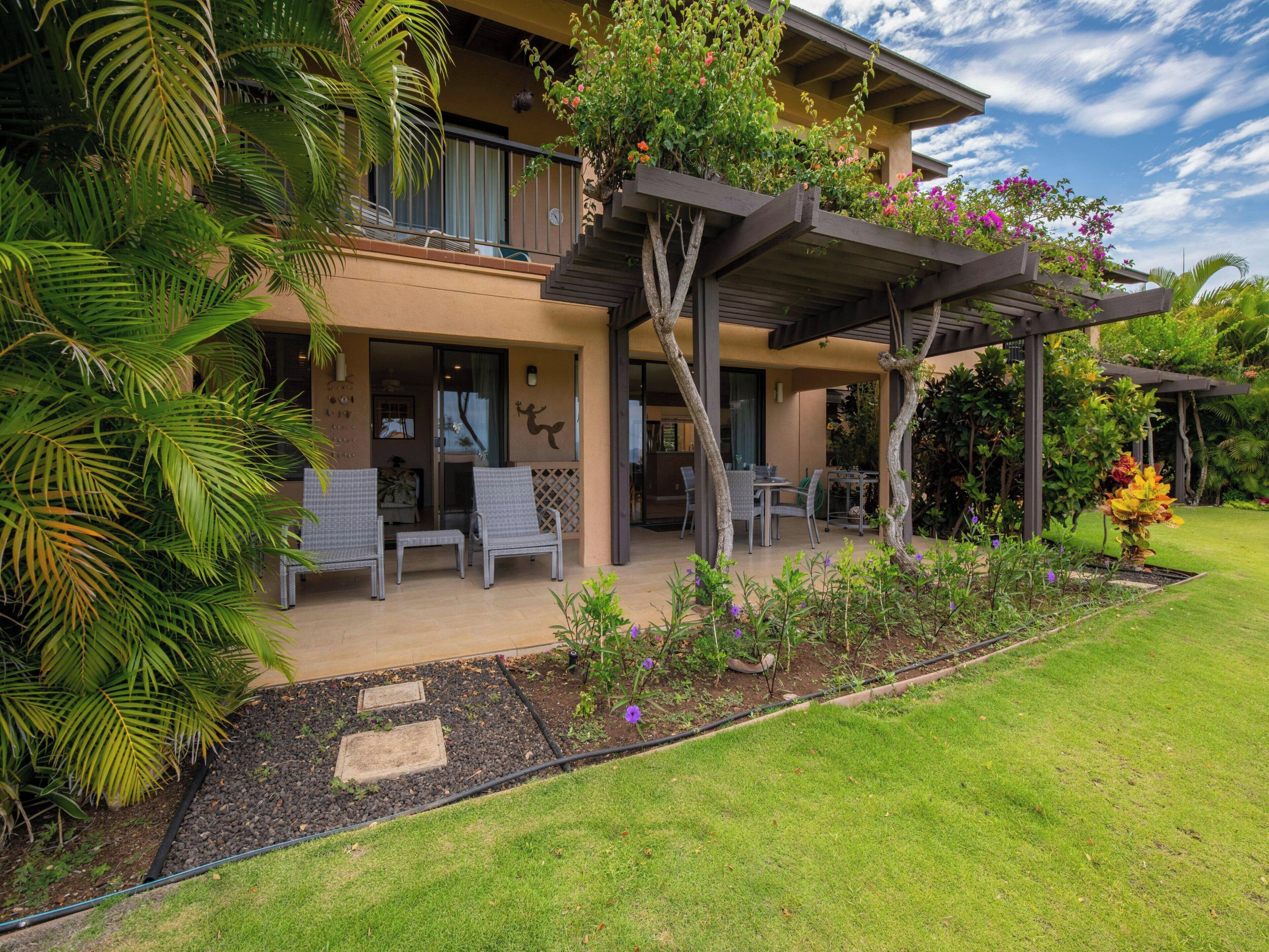 Un bâtiment à deux étages doté d’un patio couvert, d’un espace extérieur aménagé pour s’asseoir et d’un jardin où poussent diverses plantes et fleurs.