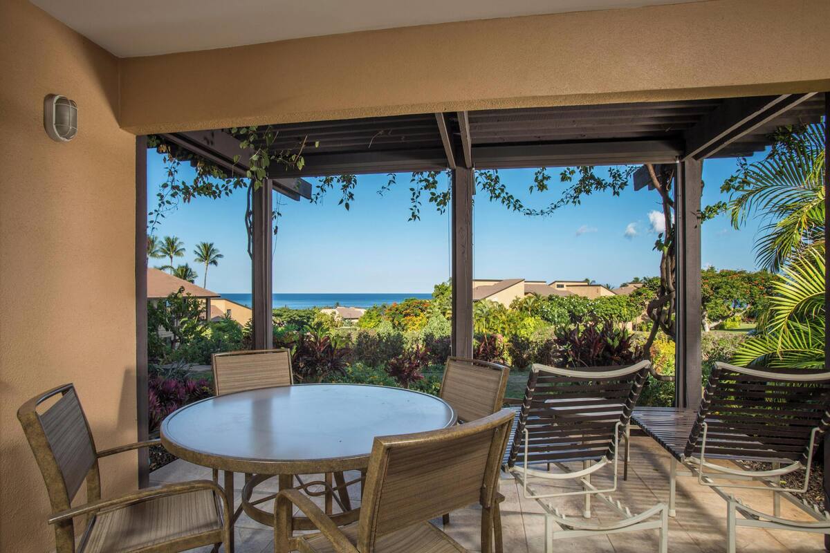Un patio con una mesa redonda y sillas, una pérgola y vistas al océano y la vegetación.