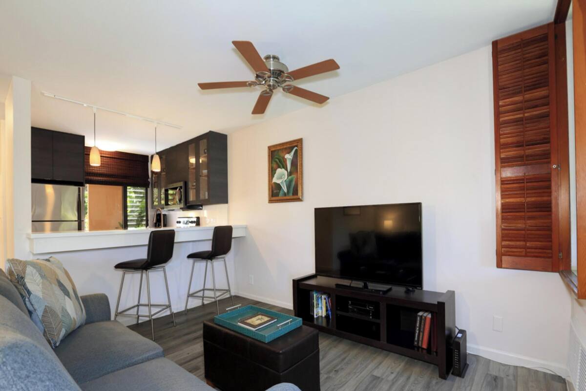 Una sala moderna con sofá, mesa de centro y mueble para televisión. Hay una zona de cocina con mesa y sillas.