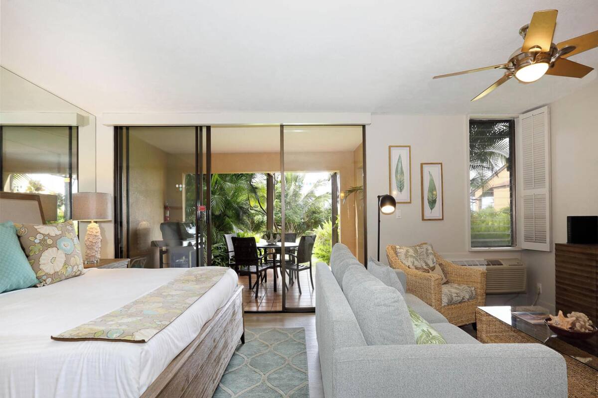 Habitación de hotel con cama, sofá, mesa de comedor con sillas, ventilador de techo y vistas al exterior.