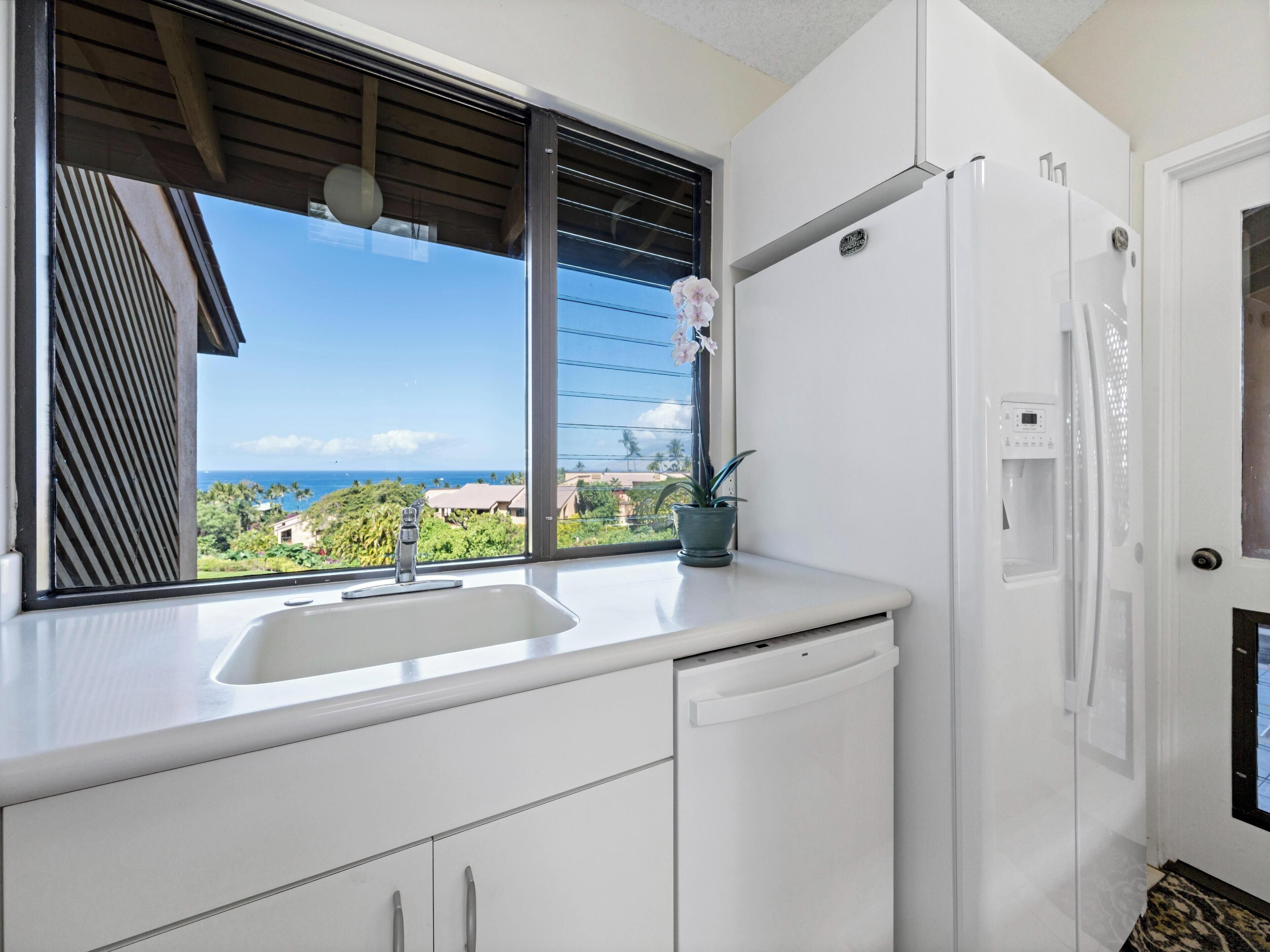Eine moderne Küche mit großem Fenster, weißen Schränken, einer integrierten Spüle und einem Kühlschrank.