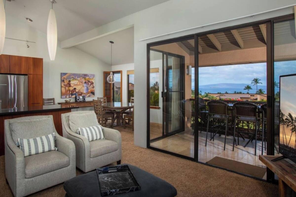 Un salón moderno con un amplio ventanal corredera que da a un balcón con vistas al océano.
