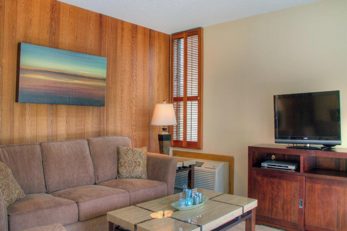 Una sala de estar con sofá, mesa de centro, televisor y paneles de madera en las paredes.