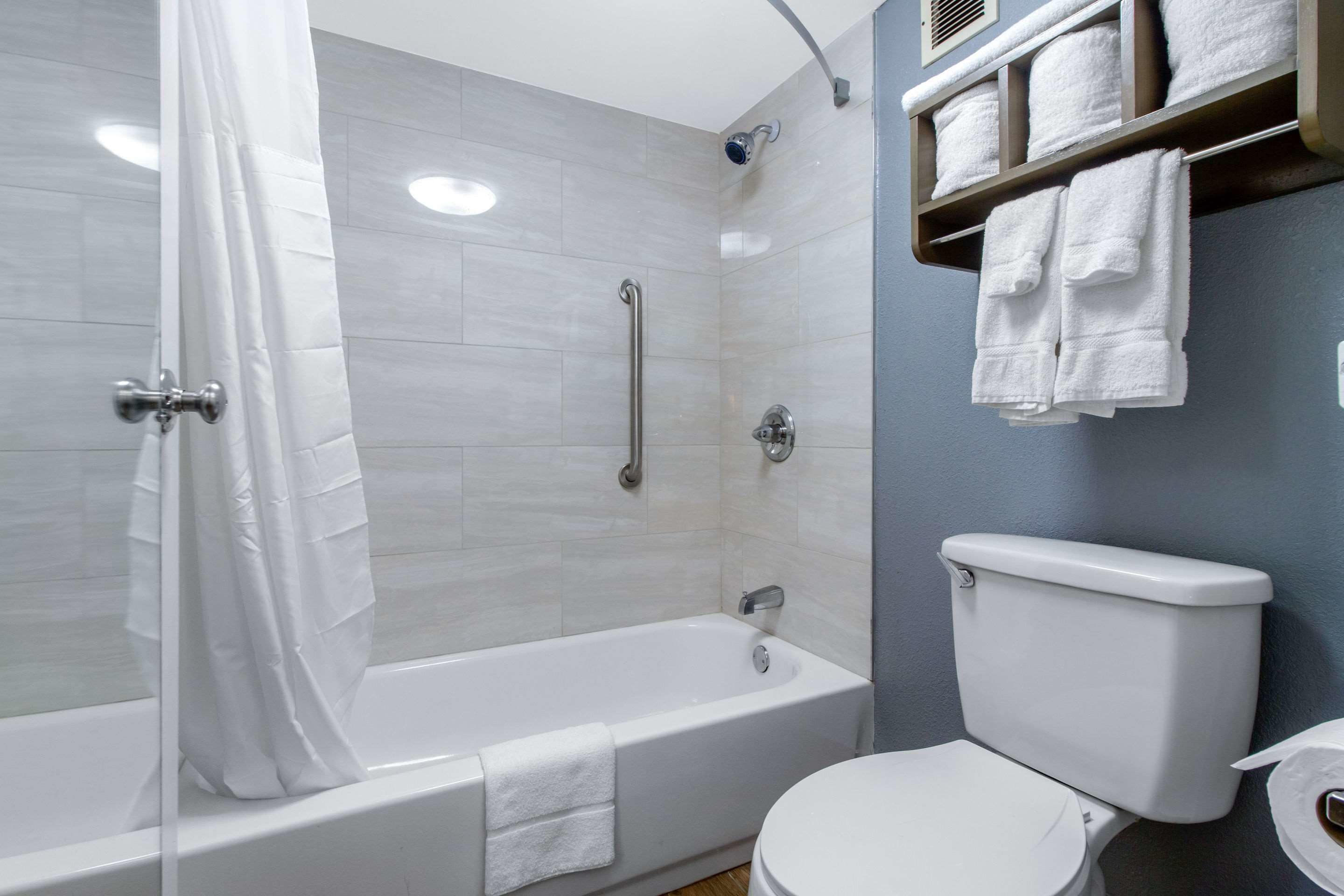 A modern bathroom with a bathtub, toilet, and a shelf with towels.