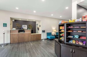 Un área de recepción con un escritorio de madera, una silla azul, un reloj y estantes llenos de aperitivos.