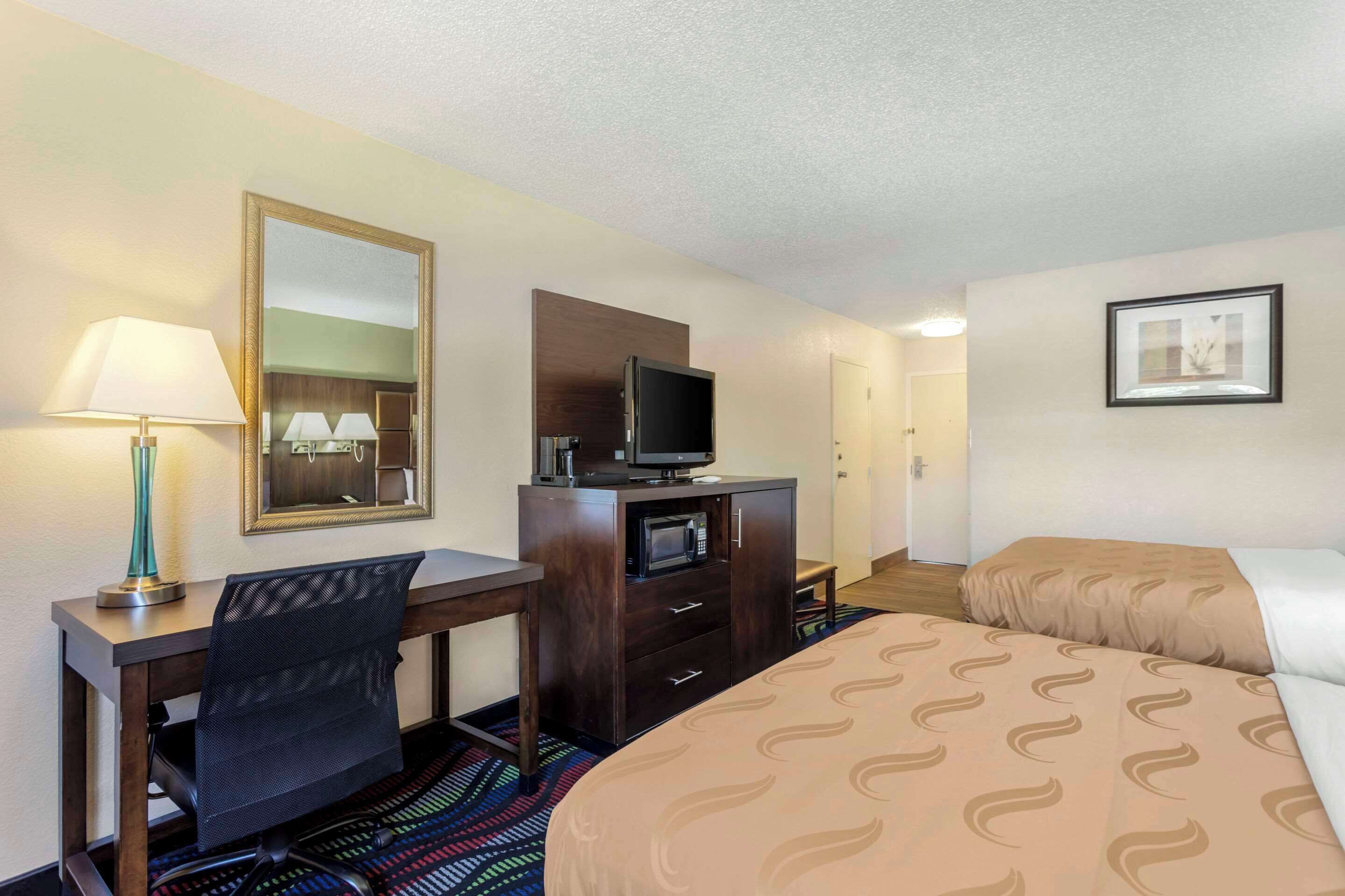 A hotel room with a bed, desk, chair, TV, and dresser.