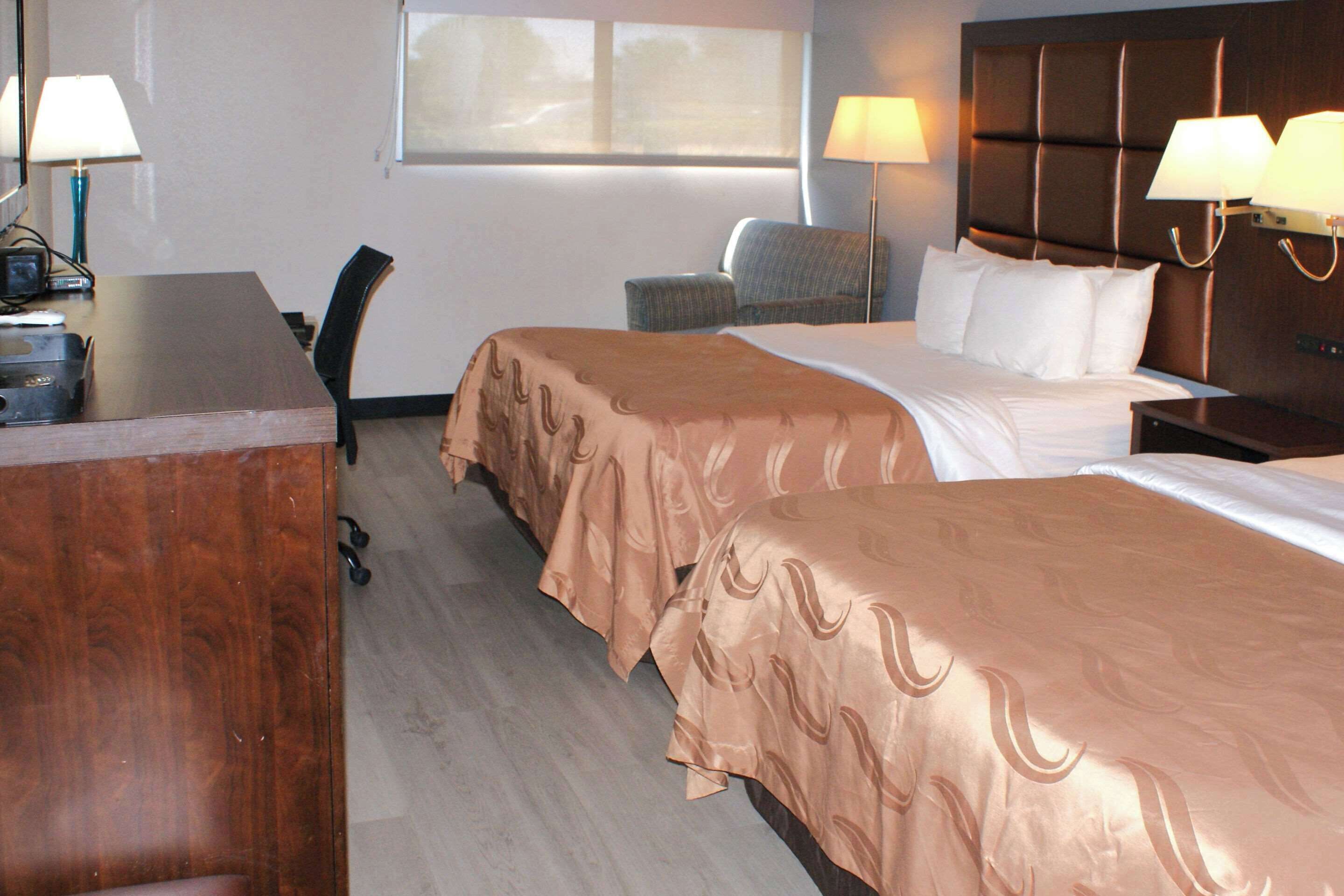 Habitación de hotel con dos camas, un escritorio, una silla y dos lámparas.
