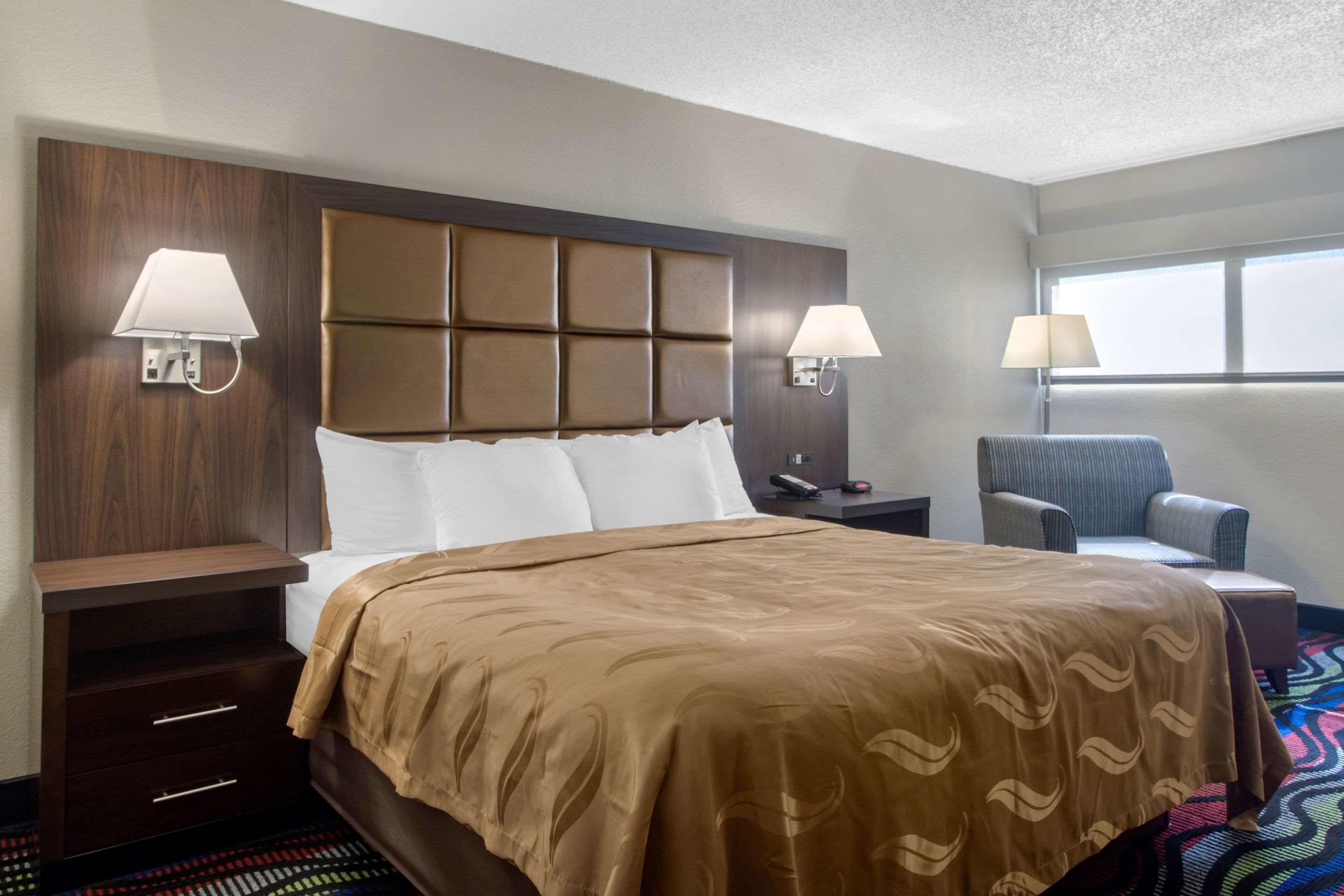 A hotel room with a large bed, two bedside lamps, a chair, and a nightstand.
