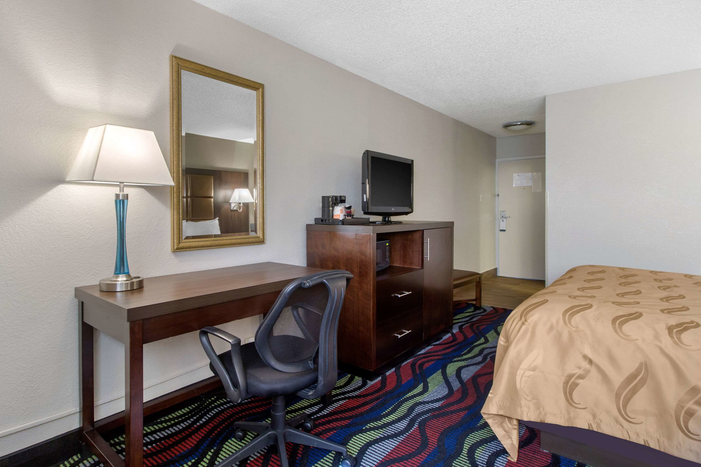 Habitación de hotel con escritorio, silla, televisión y cama con colcha estampada.