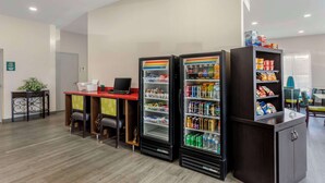 Un hall d’hôtel comprenant un comptoir d’accueil, deux distributeurs de boissons, un distributeur automatique de collations et un petit coin salon avec des chaises.
