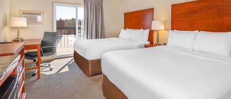 A hotel room with two beds, a desk, a chair, and a balcony with a view.