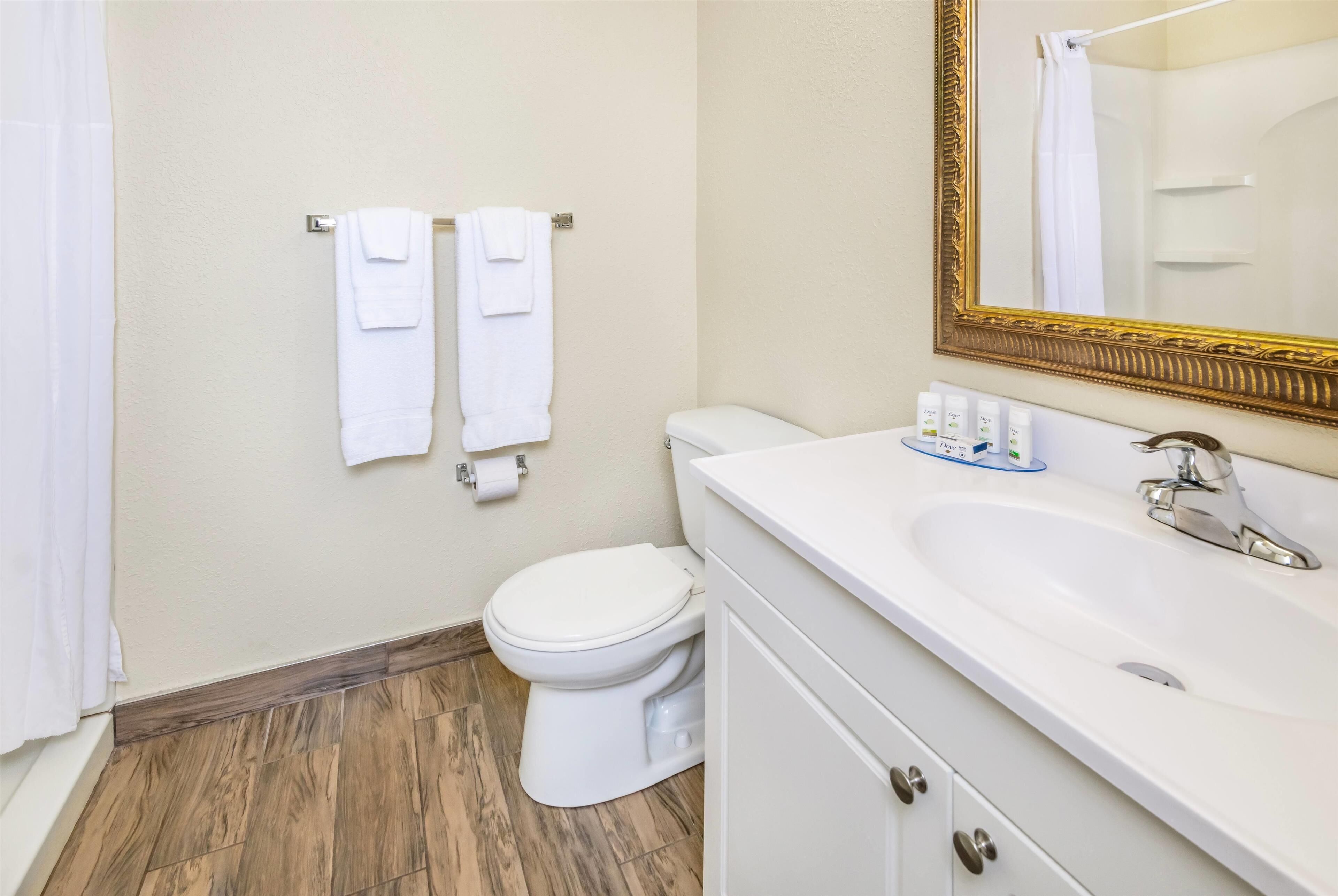 A bathroom with a white toilet, a sink with toiletries, and a mirror with a gold frame.