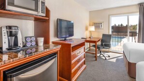 Ein Hotelzimmer mit Küchenzeile, einem Flachbildfernseher, einem Schreibtisch, einem Sessel und Blick ins Freie.