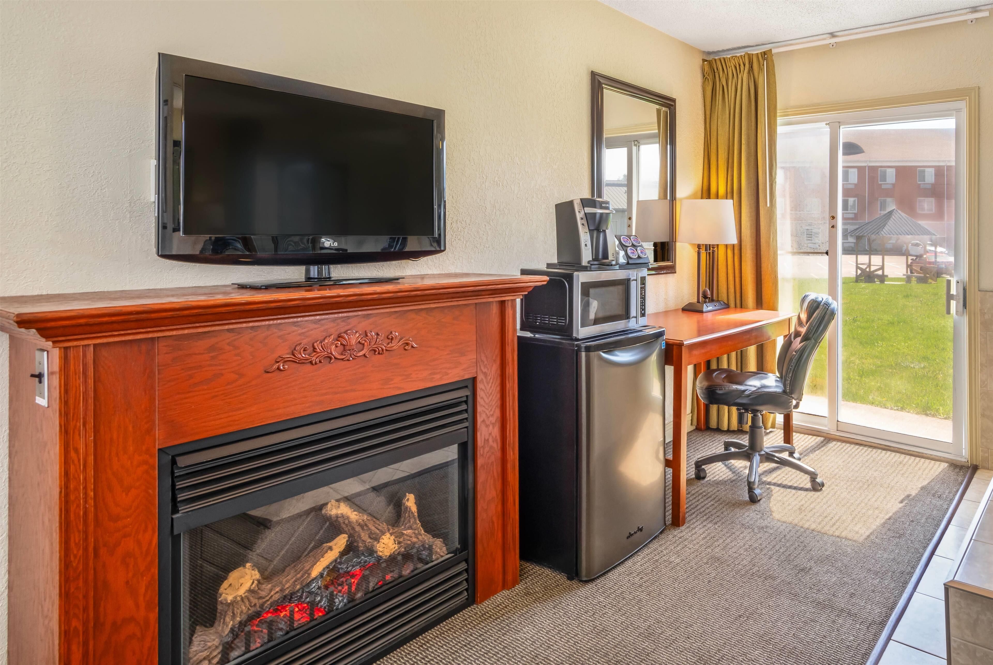A hotel room with a fireplace, a television, a desk with a lamp, a microwave, and a chair.