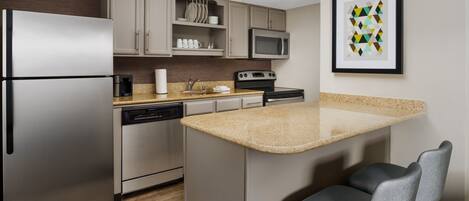 A modern kitchen with stainless steel appliances, a granite countertop, and a bar area with two chairs.