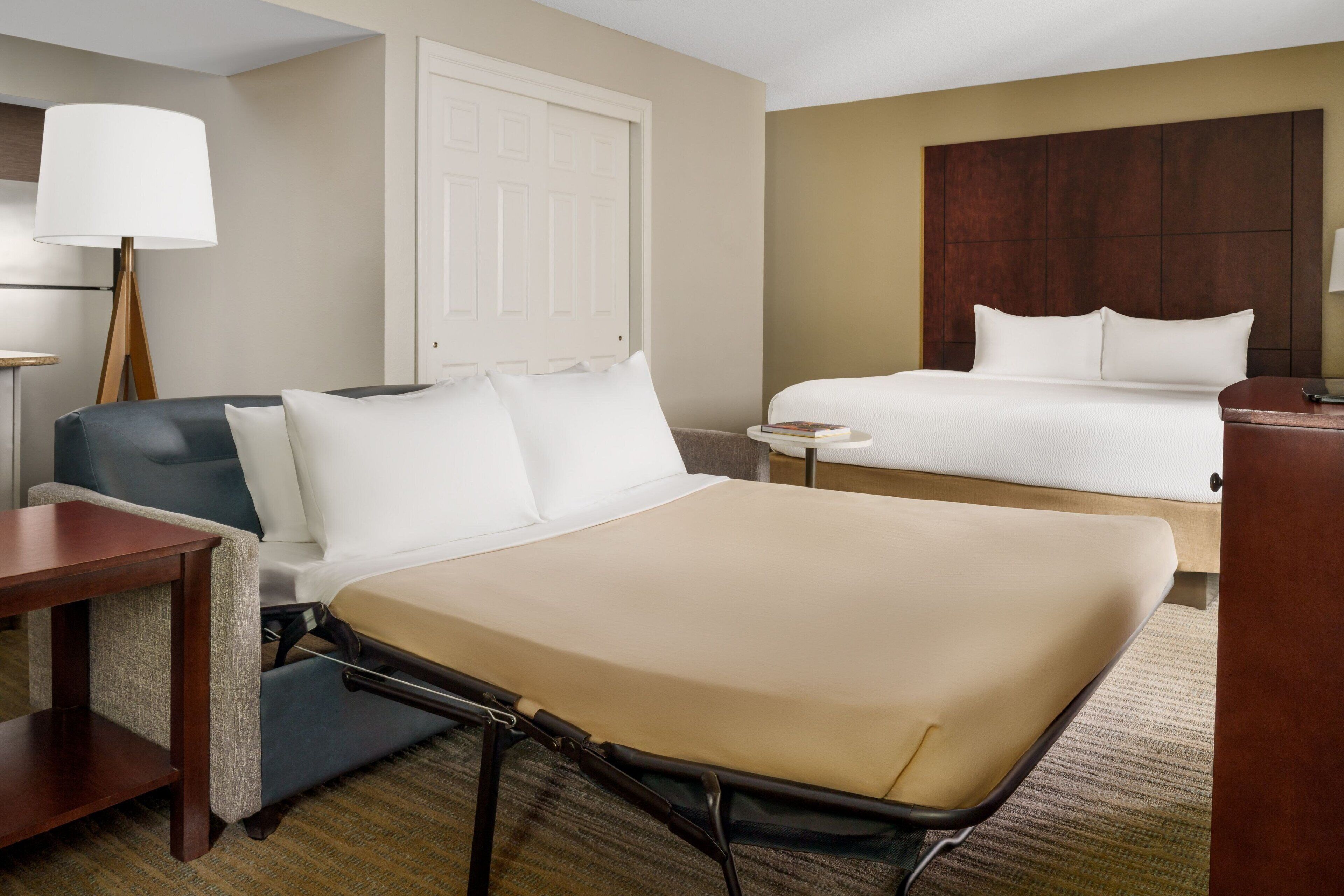 A hotel room with a single bed, a sofa, a small table, and a lamp.
