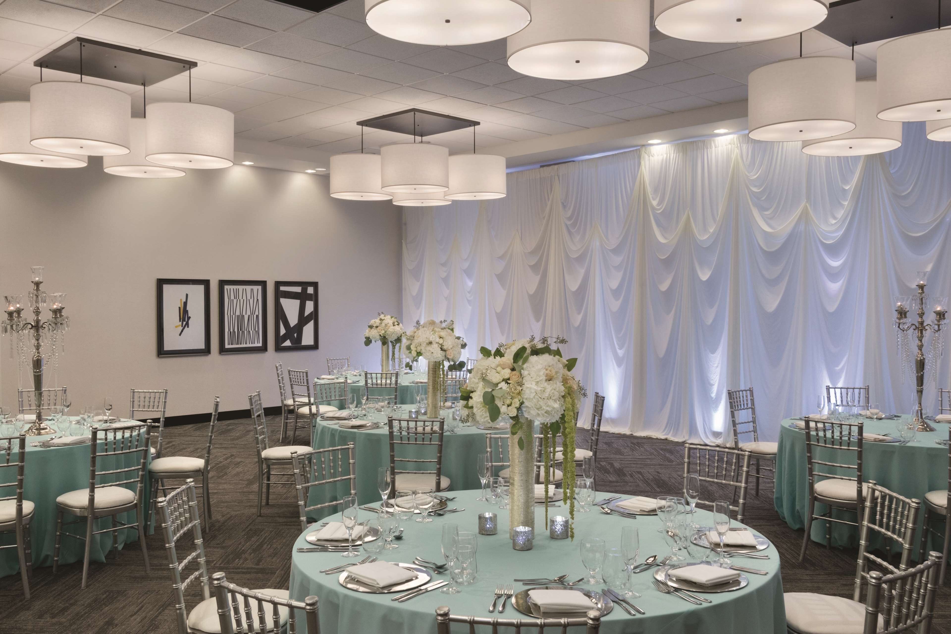 A banquet hall with round tables, white drapes, and chandeliers.
