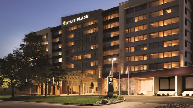 Un hotel de varios pisos con un llamativo letrero de "Hyatt Place", una entrada bien iluminada y un jardín delantero ajardinado.
