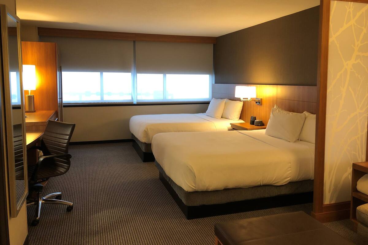 A hotel room with two beds, a desk, a chair, and a window.