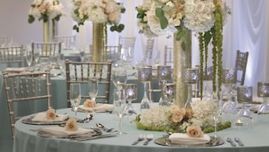 Un salón de banquetes con mesas redondas dispuestas para un evento formal, con centros de mesa florales y elegantes mantelería.
