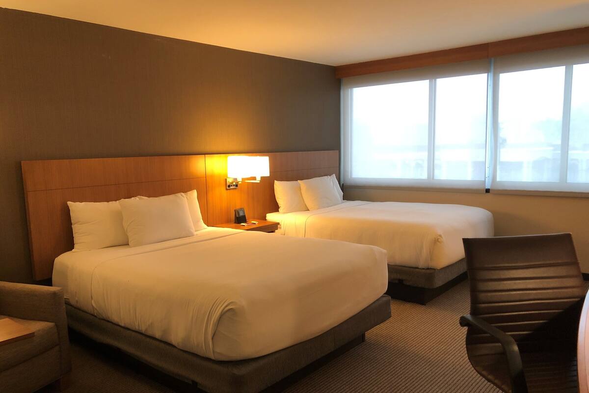 A hotel room with two beds, a desk, and a chair.