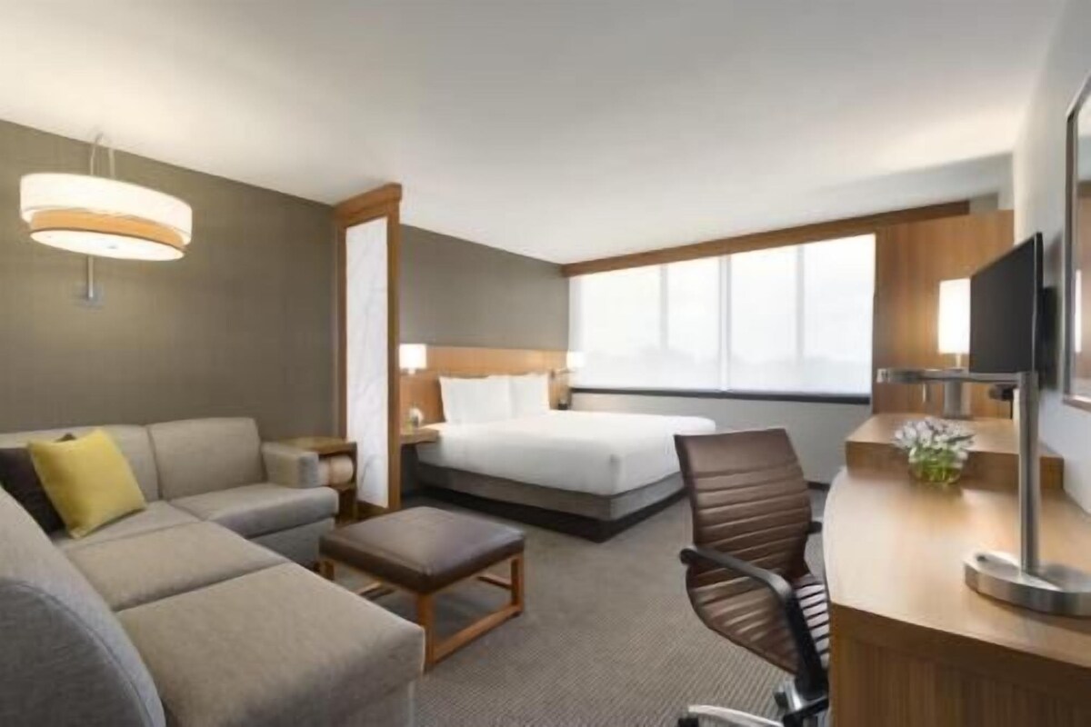 Een hotelkamer met een bed, een slaapbank, een bureau, een stoel, een televisie en een raam.