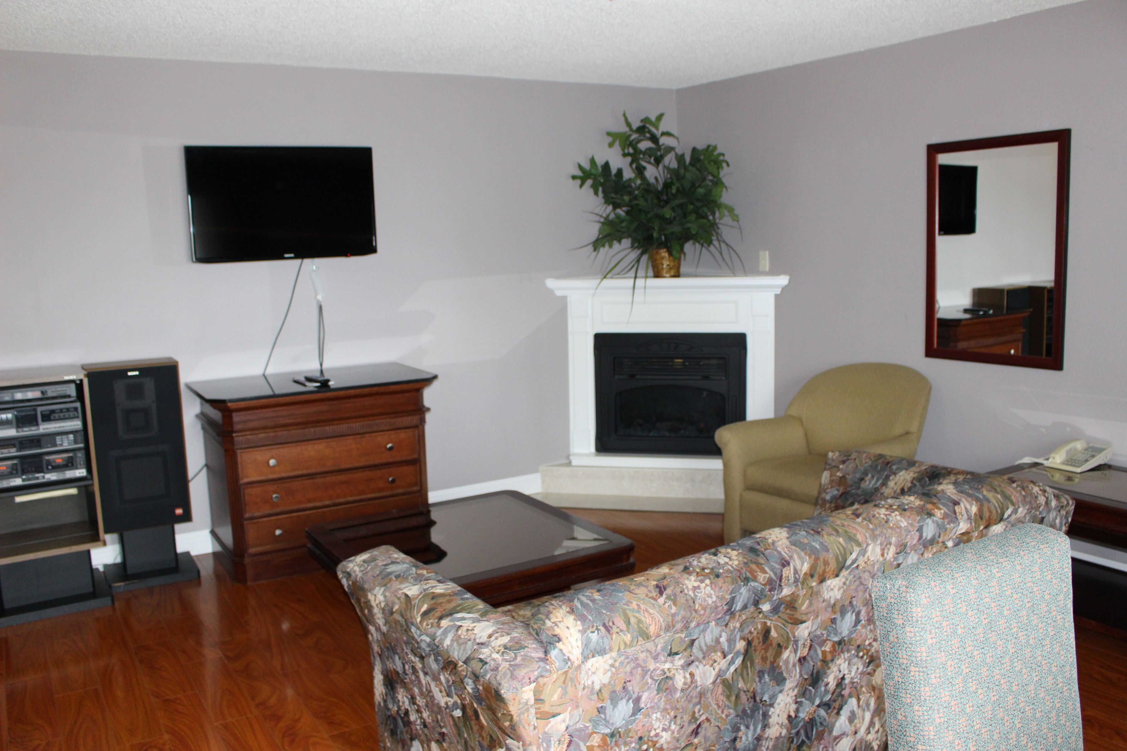 A living room with a flat-screen TV, a fireplace, a sofa, a chair, and a wooden cabinet.