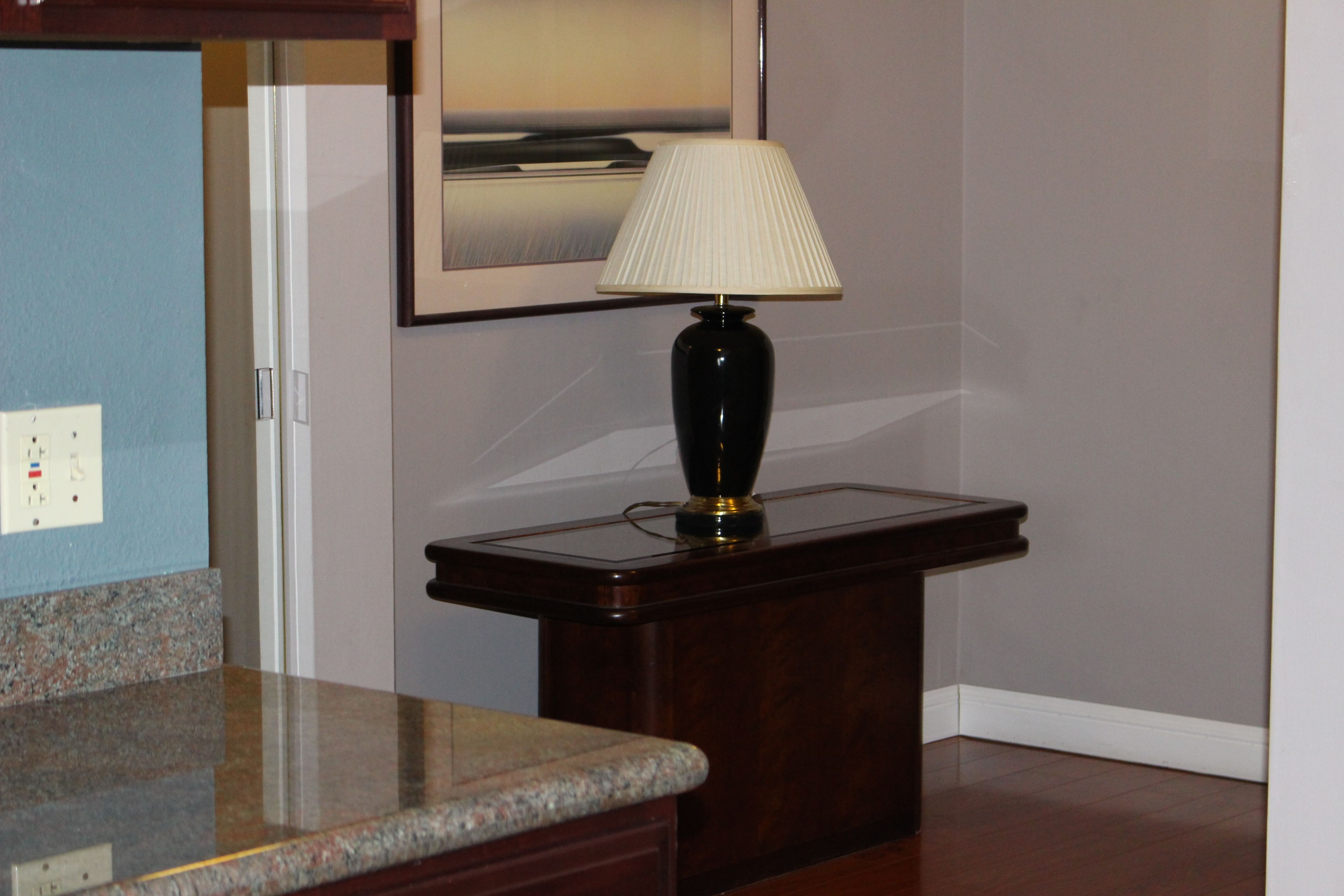 A room with a dark wooden side table, a lamp, and a framed picture on the wall.