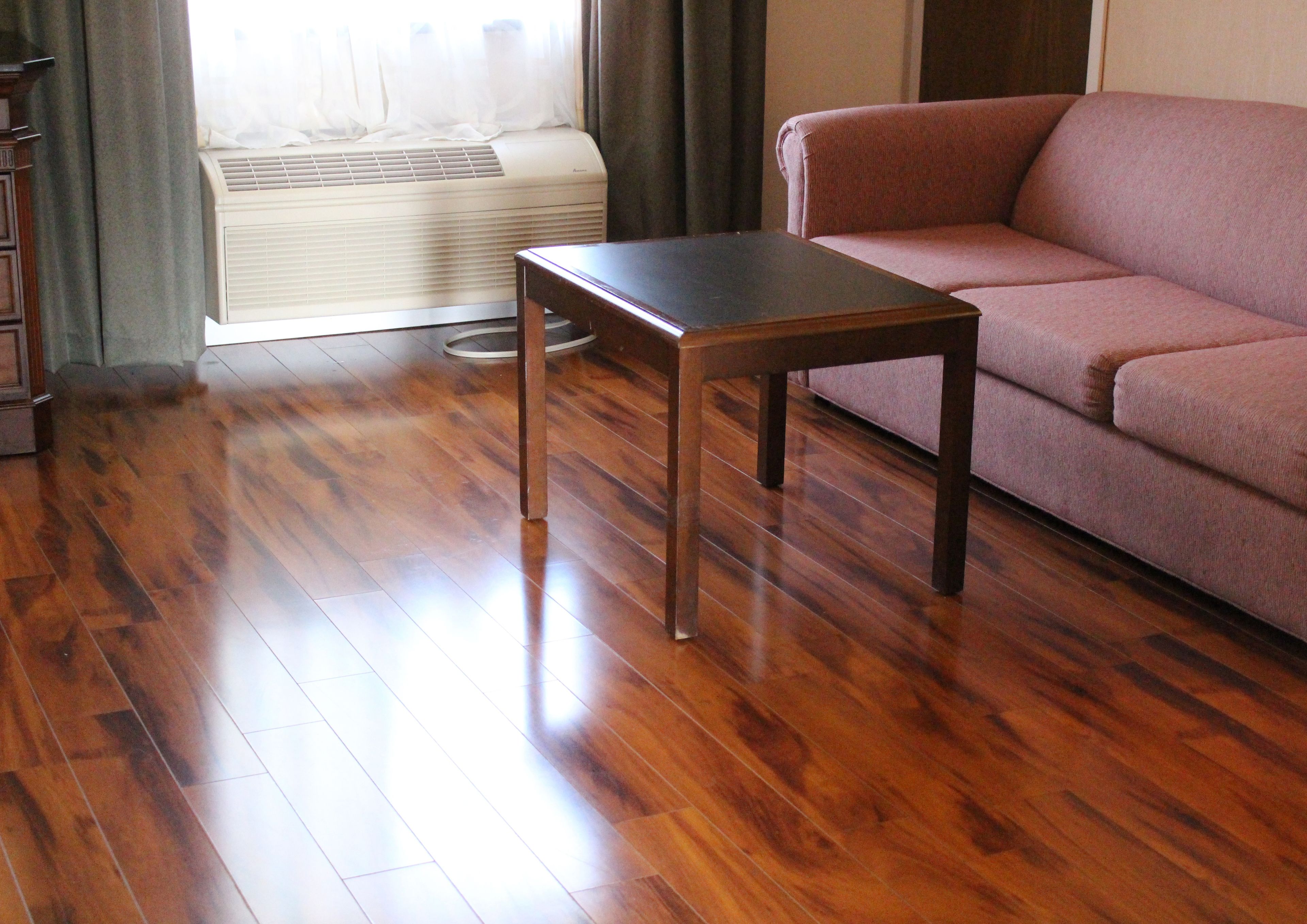 Una habitación con piso de madera, aire acondicionado color beige, una mesa de madera y un sofá rosa.