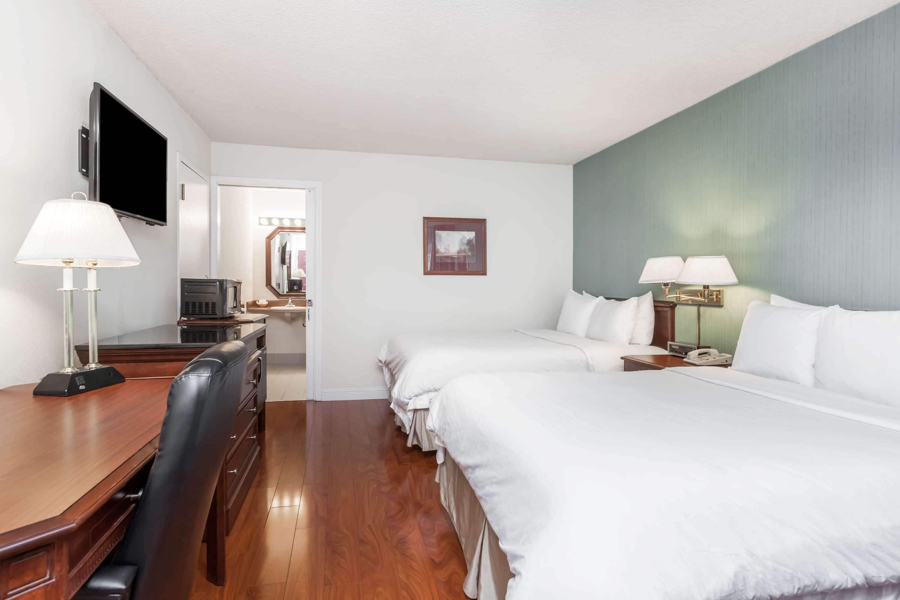 A hotel room with a wooden desk, two beds, a TV, and a mirror.